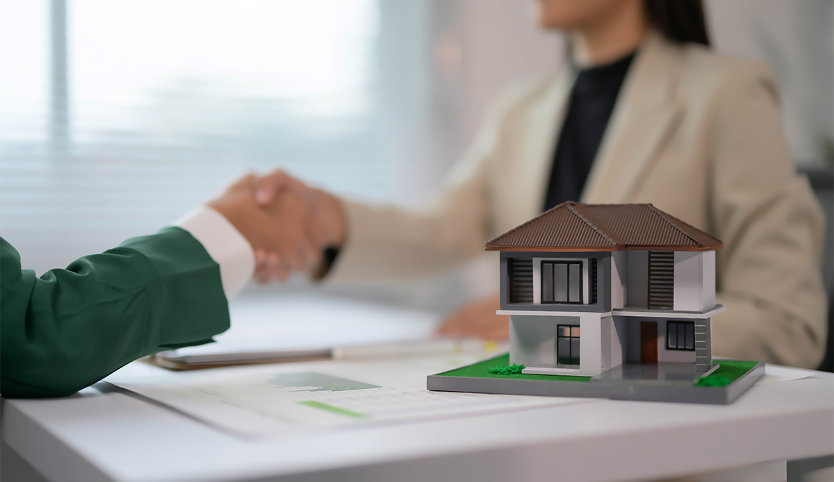 2 people shaking hands over some signed papers with a small model of a house beside them