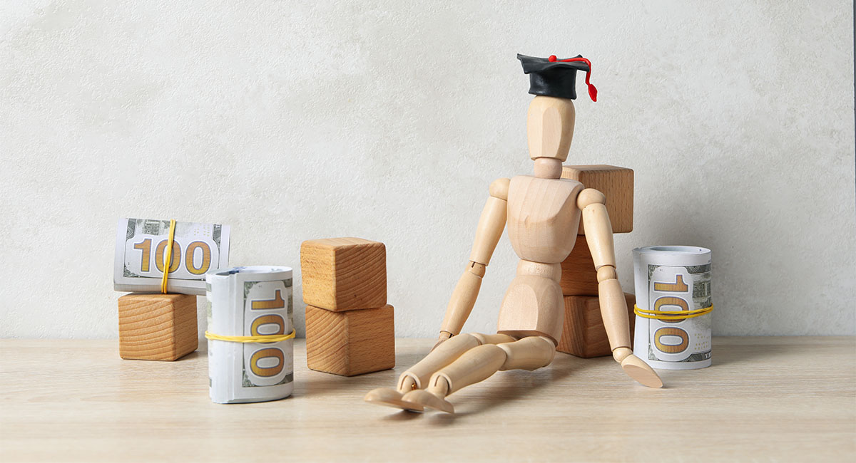 small model of a person with a graduation cap on and some rolls of money surrounding it